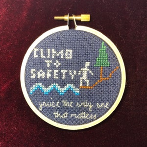 May include: A blue and white embroidered hoop with the text "Climb to Safety" and a stick figure climbing a path to a green tree. The text below the figure reads "You're the only one that matters."