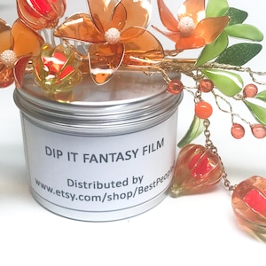 May include: A decorative floral hair accessory with orange and red translucent flowers, green leaves, and orange beads. The accessory is placed on top of a silver container with the text "DIP IT FANTASY FILM".