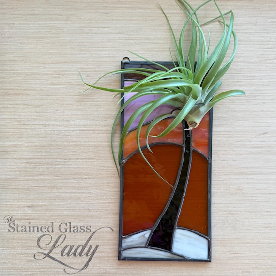 Actual hand-soldered stained glass in a moody amber-and-plum palm tree silhouette — real lead-and-glass craft that hangs in a window and glows.