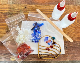 May include: A craft kit with a wooden heart-shaped frame, glass pieces in red, white, and blue, and two white bottles with red caps. Includes a small bowl, a wooden stick, and several small plastic bags.