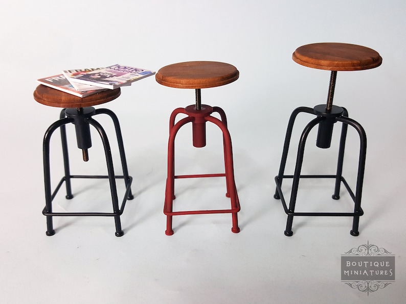 May include: Three adjustable height stools with wooden seats and metal frames. One stool is red, and the other two are black.