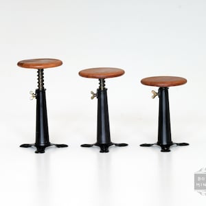 May include: Three miniature adjustable stools. Each stool has a round, wooden seat, a black metal base, and a brass-colored adjustment knob. The stools are designed to be adjustable in height.