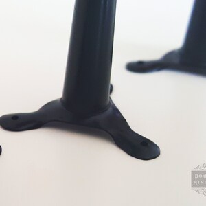 May include: Close-up of black miniature furniture legs. Each leg has a rounded, cylindrical body and a three-pronged base with a hole for attachment. The legs are set against a white background. The image is well-lit and shows the details of the legs.