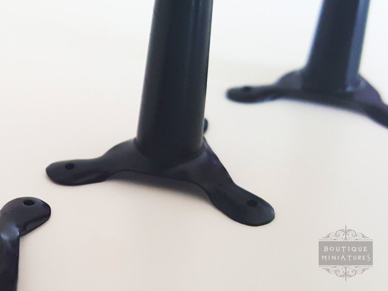 May include: Close-up of black miniature furniture legs. Each leg has a rounded, cylindrical body and a three-pronged base with a hole for attachment. The legs are set against a white background. The image is well-lit and shows the details of the legs.