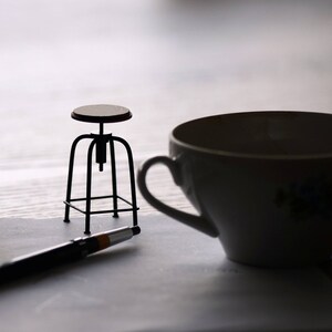 May include: A black metal stool with a wooden seat, a white teacup, and a black pen on a white surface.