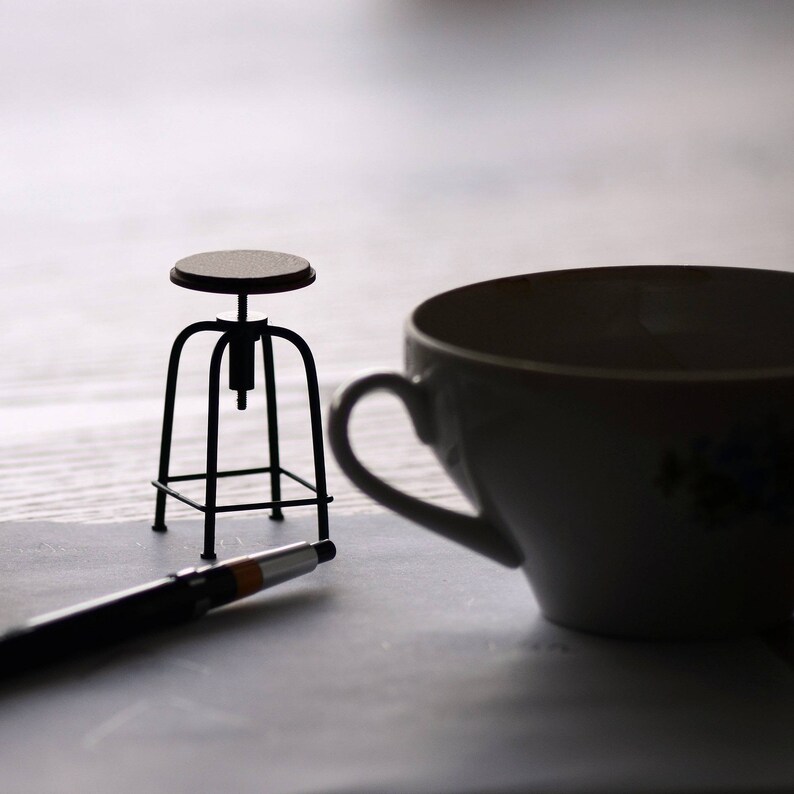May include: A black metal stool with a wooden seat, a white teacup, and a black pen on a white surface.