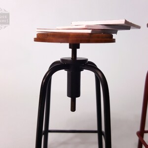 May include: A black metal bar stool with a wooden seat and a screw adjustment mechanism. The stool is topped with a stack of white paper.