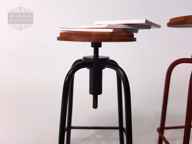 May include: A black metal bar stool with a wooden seat and a screw adjustment mechanism. The stool is topped with a stack of white paper.