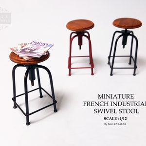 May include: Three miniature French industrial swivel stools. One stool is black with a wooden seat and has a stack of magazines on top. The other two stools are red and black with wooden seats.