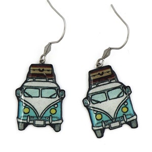 Peut inclure: Une paire de boucles d'oreilles pendantes représentant un van vintage bleu et blanc avec un porte-bagages et une valise brune sur le toit. Le van a des phares jaunes et un pare-brise blanc. Les boucles d'oreilles sont en métal avec une finition argentée.