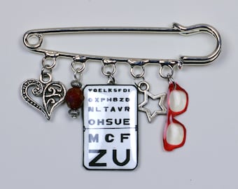 Silver pin brooch, reading test, Monoyer scale, pair of glasses, silver heart, red glass bead