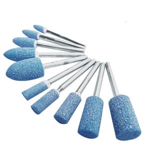 Puede incluir: Un conjunto de diez puntas abrasivas de color azul con vástagos metálicos, dispuestas en abanico. La colección incluye varias formas, como cabezales puntiagudos, de bala y cilíndricos, todos con una superficie rugosa y texturizada.
