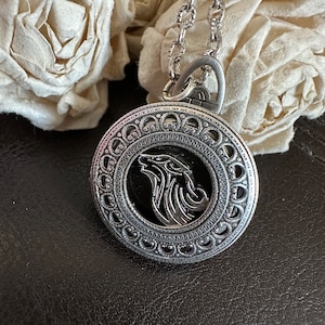 May include: Silver necklace with a round pendant featuring a wolf's head design. The pendant has a detailed, ornate border.