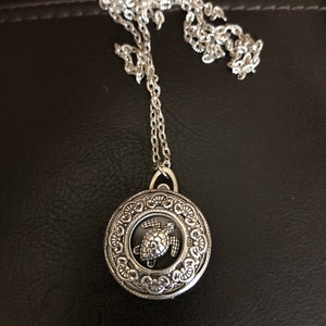 May include: Silver necklace with a round pendant featuring a detailed turtle design.