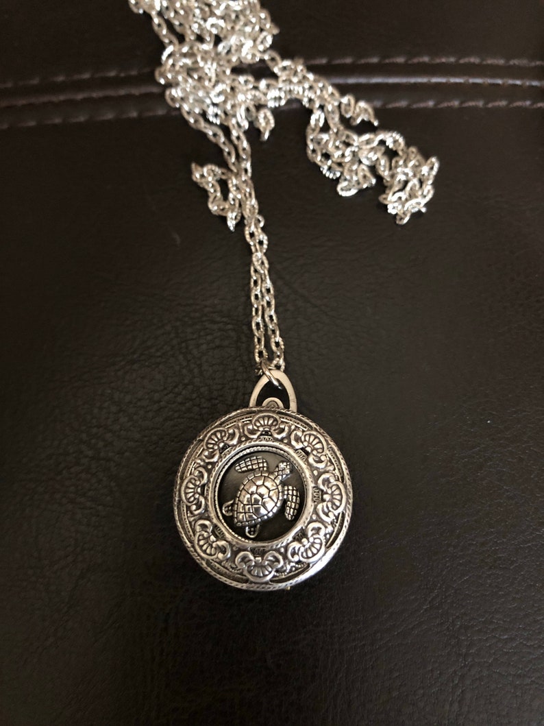 May include: Silver necklace with a round pendant featuring a detailed turtle design.
