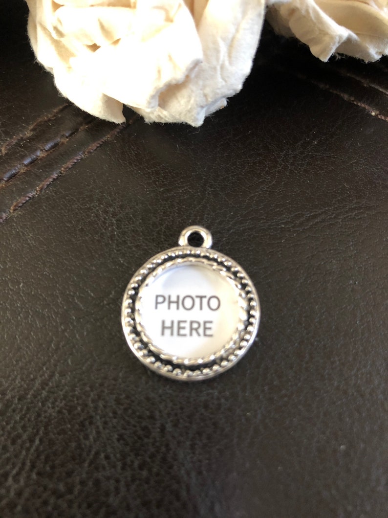 K&ouml;nnte beinhalten: Silberner Anh&auml;nger mit einem runden Fotorahmen, auf dem in schwarzer Schrift "FOTO HIER" steht.