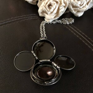 May include: A silver locket necklace with three hinged compartments. The locket is open, revealing a small, round, brown interior.
