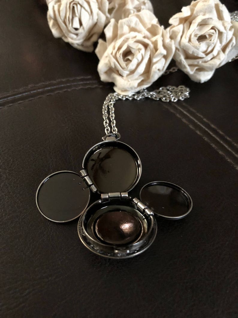 May include: A silver locket necklace with three hinged compartments. The locket is open, revealing a small, round, brown interior.