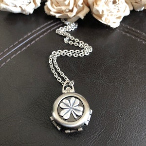 May include: A silver necklace with a round pendant featuring a four-leaf clover design. The pendant has a black background and the clover is raised and detailed.