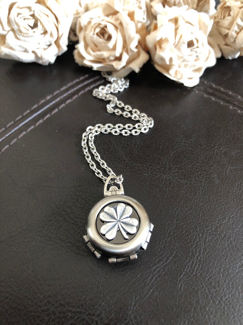May include: A silver necklace with a round pendant featuring a four-leaf clover design. The pendant has a black background and the clover is raised and detailed.