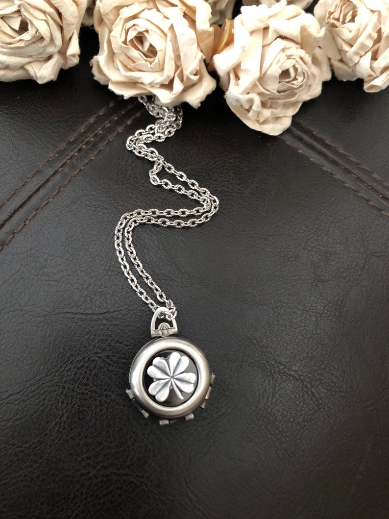 May include: A silver chain necklace with a round pendant featuring a four-leaf clover design.
