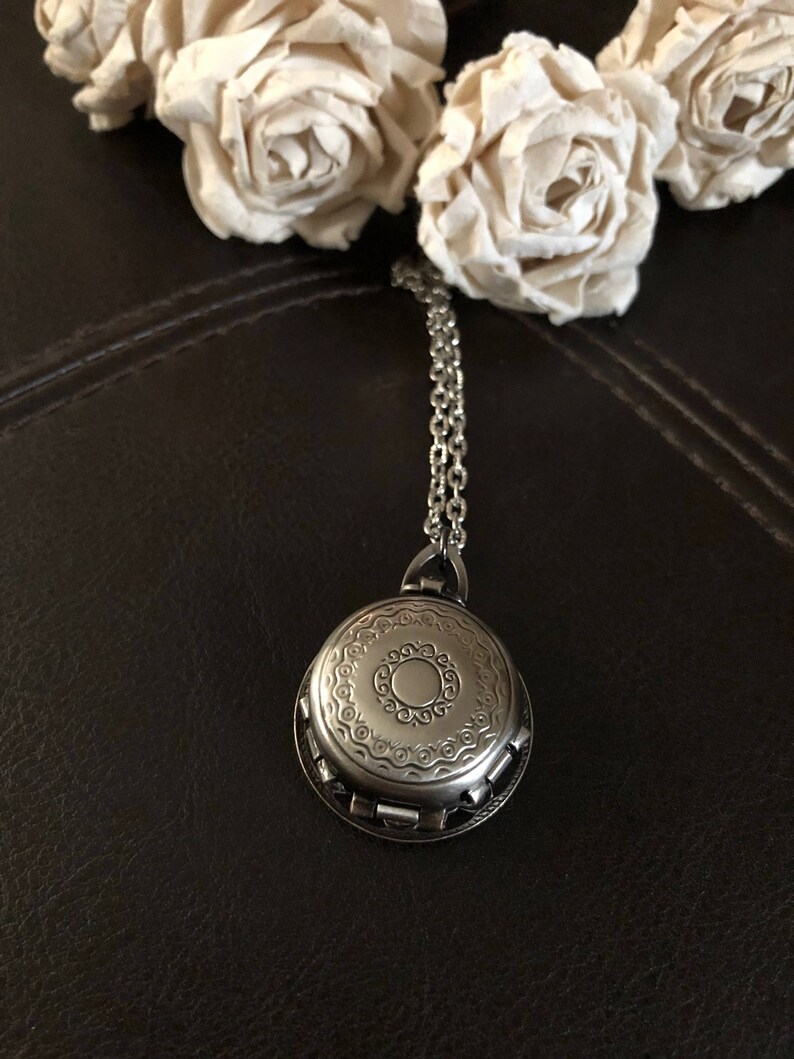 May include: A silver locket necklace with an ornate design. The locket is circular and features a repeating pattern of circles and swirls. The necklace is made of a silver chain.