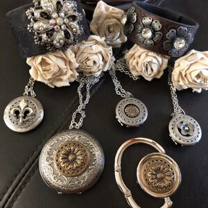 May include: A set of five silver and gold tone jewellery pieces with floral designs. The set includes two leather bracelets, a locket, a charm, and a purse hook.