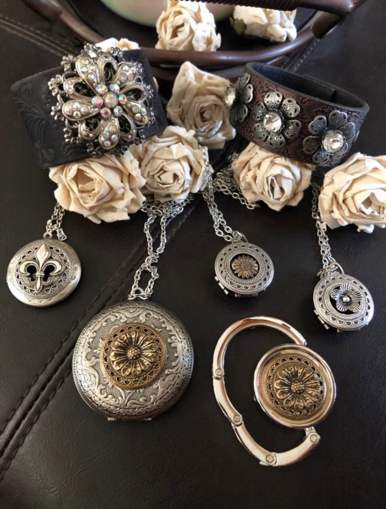 May include: A set of five silver and gold tone jewellery pieces with floral designs. The set includes two leather bracelets, a locket, a charm, and a purse hook.