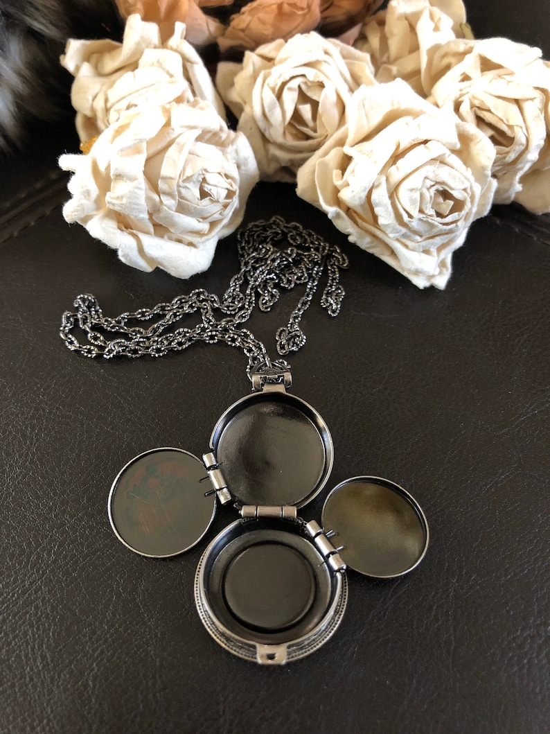 May include: A silver locket necklace with three hinged compartments. The locket is open, revealing the empty interior of each compartment.