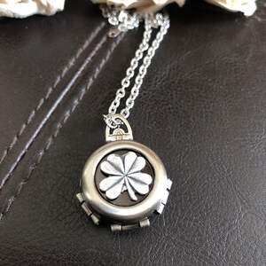May include: A silver necklace with a four-leaf clover pendant. The pendant is round and has a black background. The clover is silver and raised.
