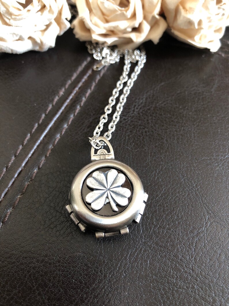 May include: A silver necklace with a four-leaf clover pendant. The pendant is round and has a black background. The clover is silver and raised.