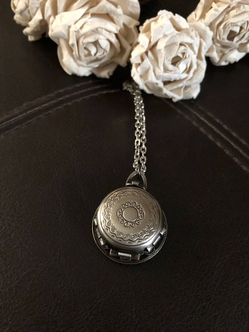 May include: A silver locket necklace with an ornate design. The locket has a circular shape and is decorated with a repeating pattern of circles and swirls. The necklace is made of a silver chain.