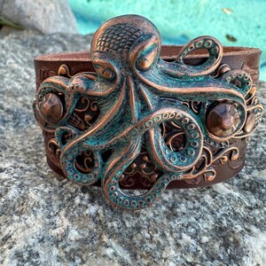 May include: A brown leather cuff bracelet with a large, detailed copper octopus design. The octopus is textured and has a green patina finish.