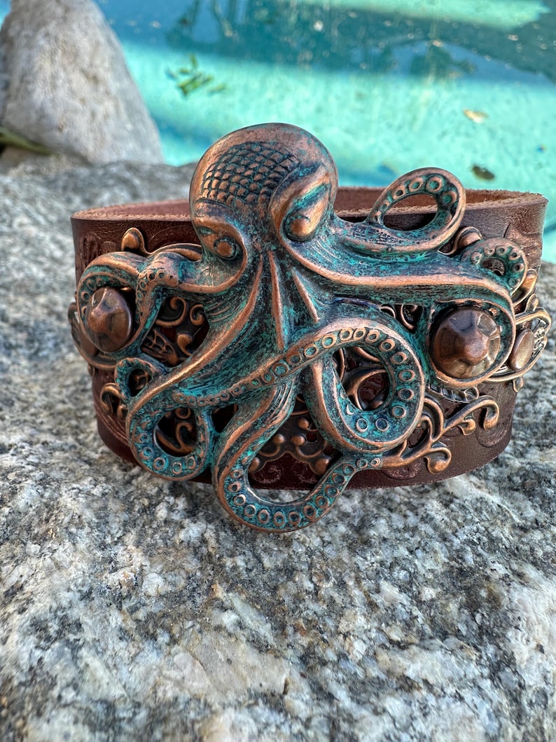 May include: A brown leather cuff bracelet with a large, detailed copper octopus design. The octopus is textured and has a green patina finish.