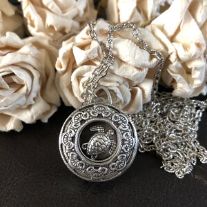 May include: A silver necklace with a round pendant featuring a detailed design of a sea turtle. The pendant is surrounded by a decorative border.