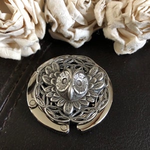 May include: Silver-toned owl-shaped purse clasp with intricate floral details. The clasp is closed and features a detailed owl head with large eyes.