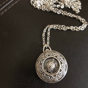 May include: A silver chain necklace with a round pendant featuring an ornate design and a silver turtle charm.