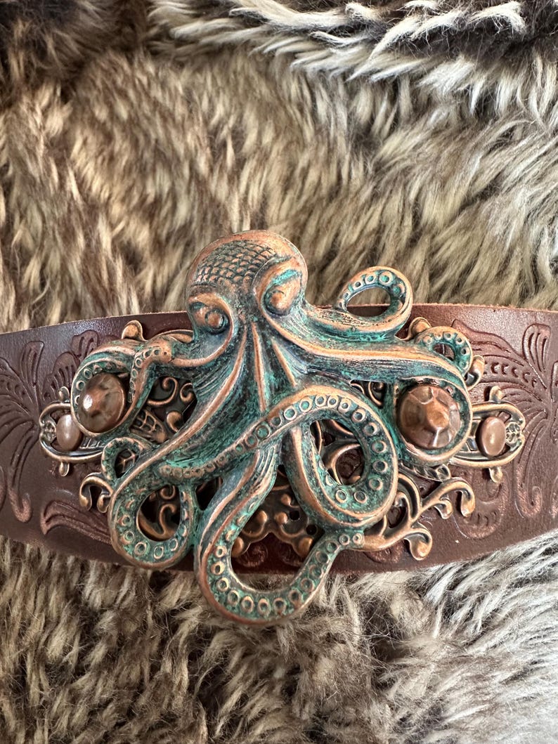 May include: A brown leather belt with an ornate metal buckle featuring a green and copper octopus design.