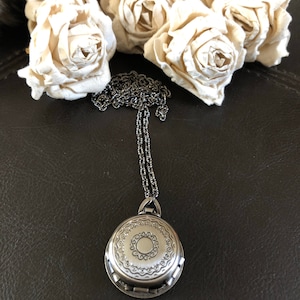 May include: A silver locket necklace with an ornate design. The locket is round and has a detailed pattern around the edge. The chain is silver and has a delicate design.