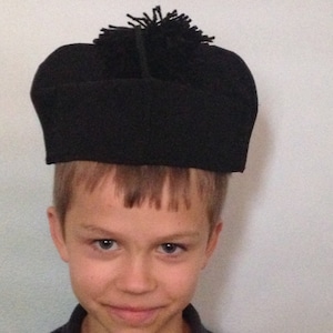 May include: A young person wearing a black hat with a black pom-pom on top.