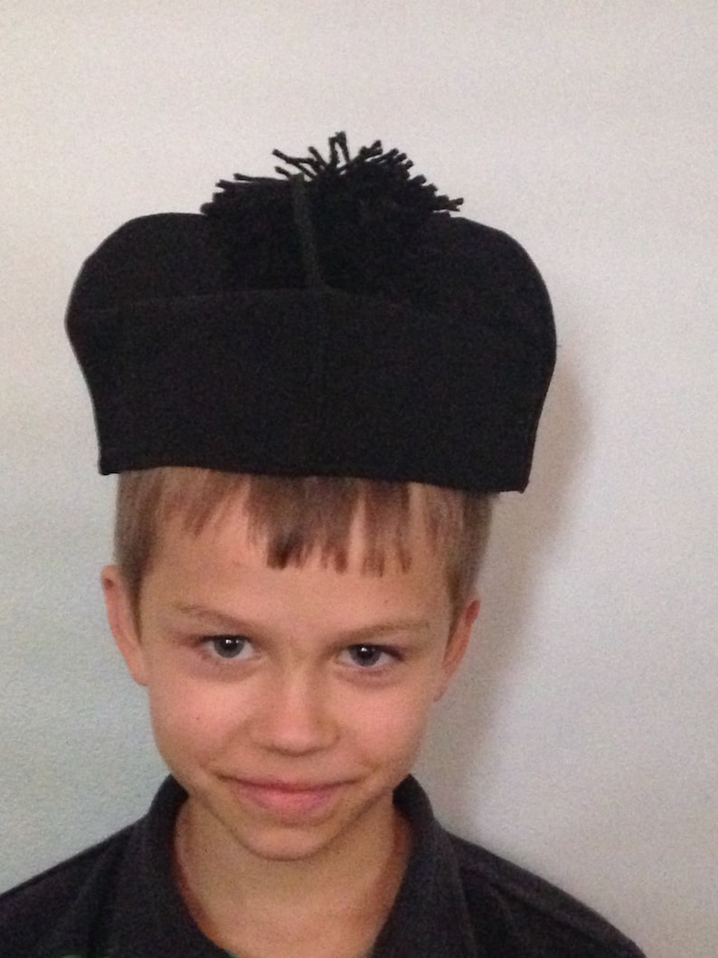 May include: A young person wearing a black hat with a black pom-pom on top.