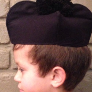 May include: A young person wearing a black felt hat with a black pom-pom on top. The hat is worn low on the forehead.