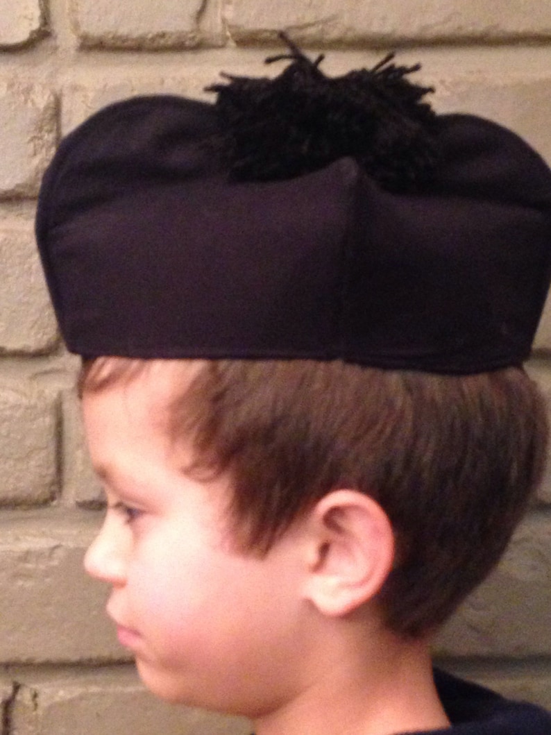 May include: A young person wearing a black felt hat with a black pom-pom on top. The hat is worn low on the forehead.