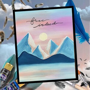 May include: A rectangular canvas painting featuring a mountain landscape with a pale yellow sun against a pink and blue gradient sky. The text "free indeed" is written in black cursive script above the mountains, which are painted in shades of blue.