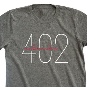 May include: A heather gray t-shirt with the number 402 printed in white. The word "remarkable" is written in red cursive underneath the number.