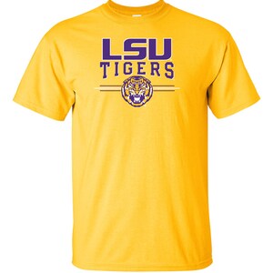 Puede incluir: Una camiseta amarilla con las palabras "LSU TIGERS" en letras moradas y un logotipo de cabeza de tigre morado.