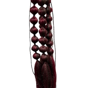 Könnte beinhalten: Eine lange, dunkelbordeauxfarbene Haarverlängerung mit mehreren Reihen kleiner, runder, bordeauxfarbener Perlen. Die Haarverlängerung ist mit einer schwarzen Schnur gebunden.