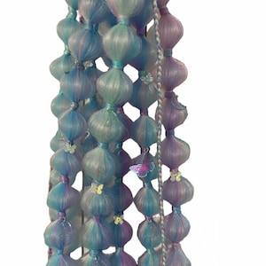 以下が含まれることがあります： 蝶のチャームが付いた青と紫のヘアエクステンションのセット。エクステンションは一連の結び目で一緒に結ばれており、カスケード効果を生み出しています。