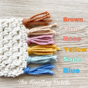 Pu&ograve; includere: Primo piano di un pezzo di uncinetto bianco con frange colorate. Le frange sono di colore marrone, beige, rosa, giallo, salvia e blu. Il testo "The Knotting Perch" &egrave; visibile nella parte inferiore dell'immagine.