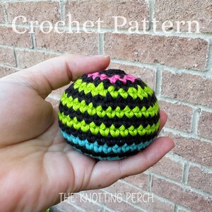 May include: A spherical crochet object featuring horizontal stripes in black, lime green, bright pink, and turquoise. The text Crochet Pattern and The Knotting Perch are visible in white lettering against the background of a brick wall.